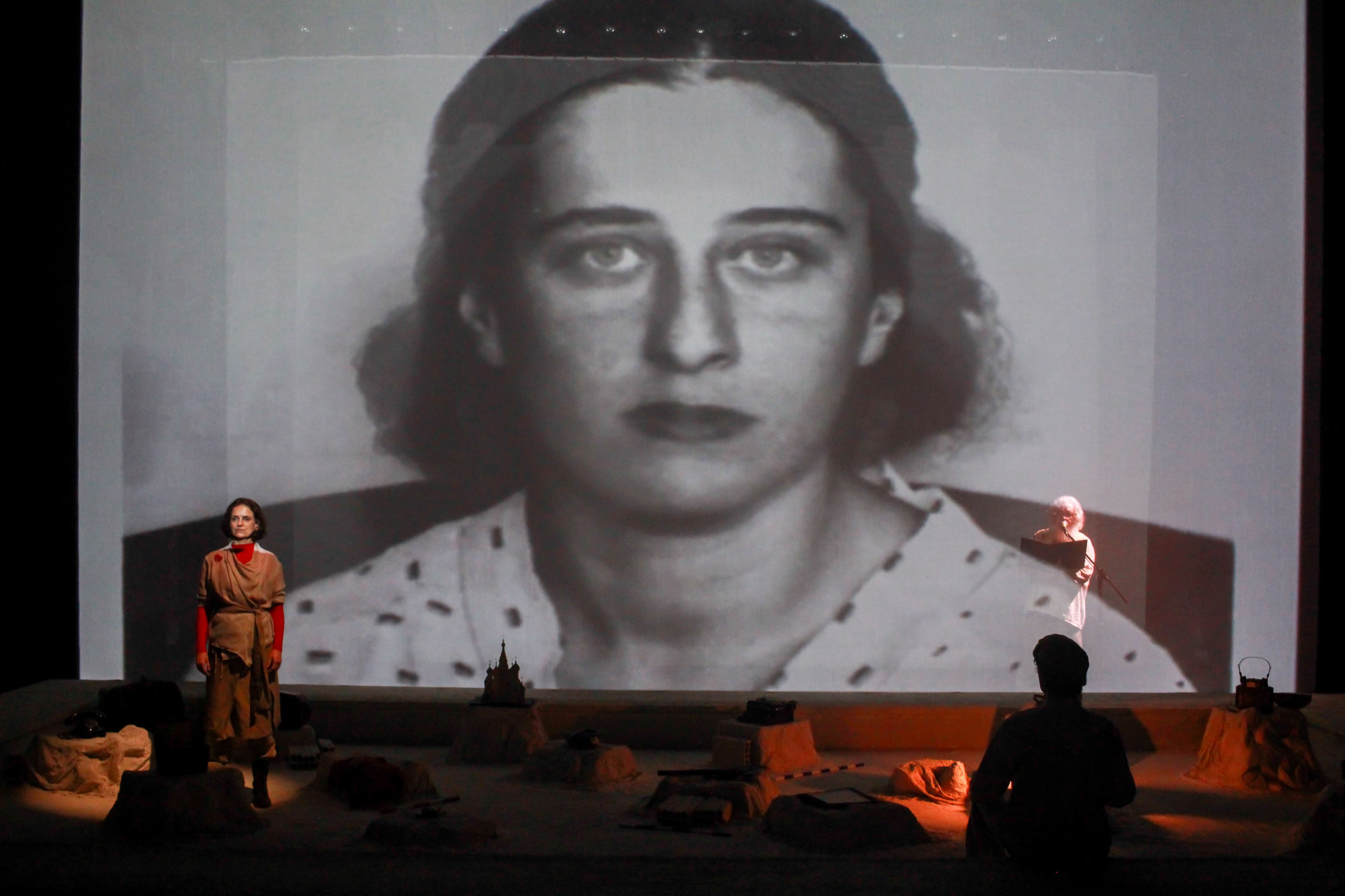 Atriz em cena diante do retrato de Olga Benario Prestes projetado nas telas sobrepostas do espetáculo