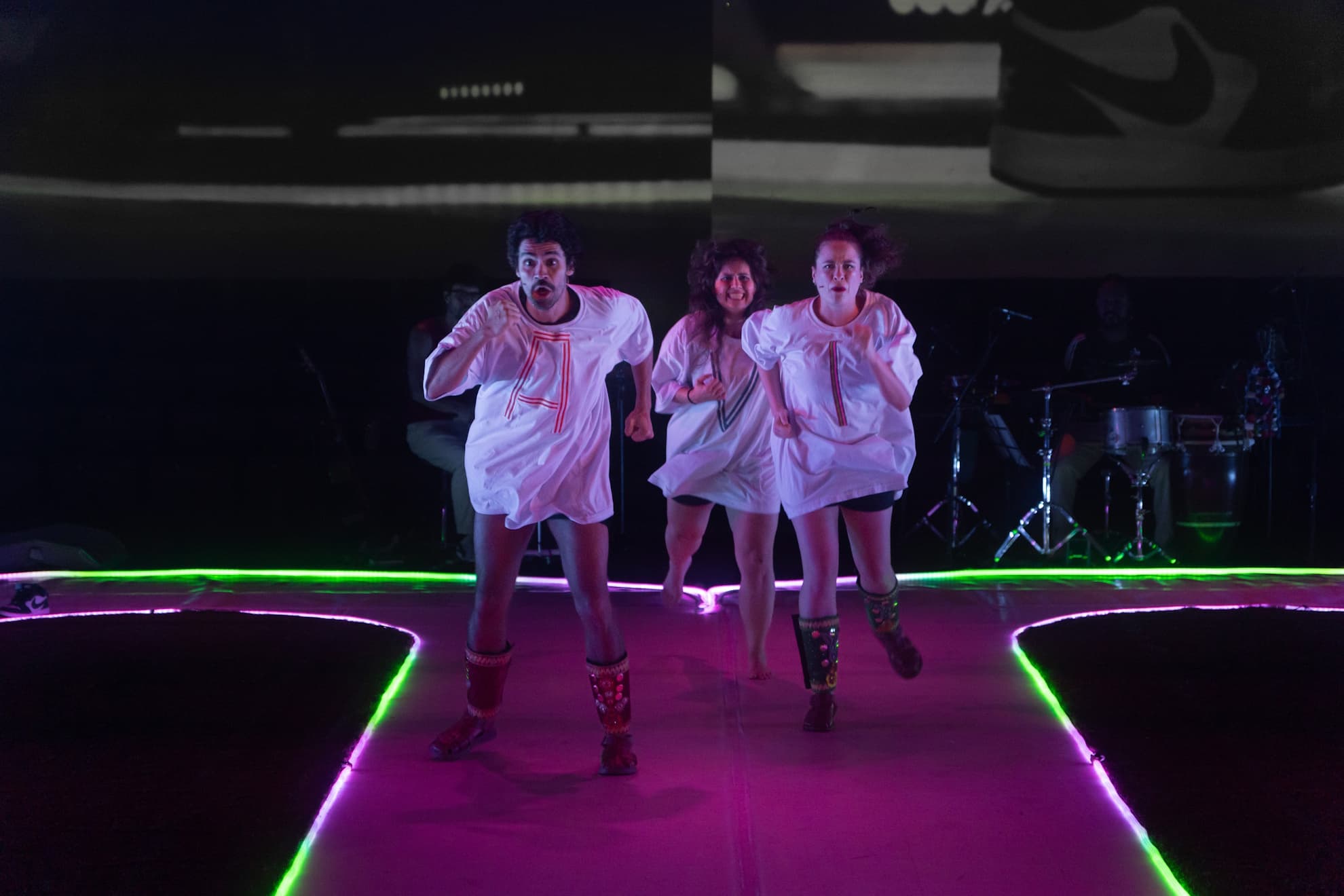 Cena de Pés-Coração com três intérpretes correndo pelas pistas do palco.